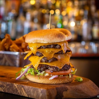 A burger with multiple layers of cheese and patties at Fable Craft Bar.